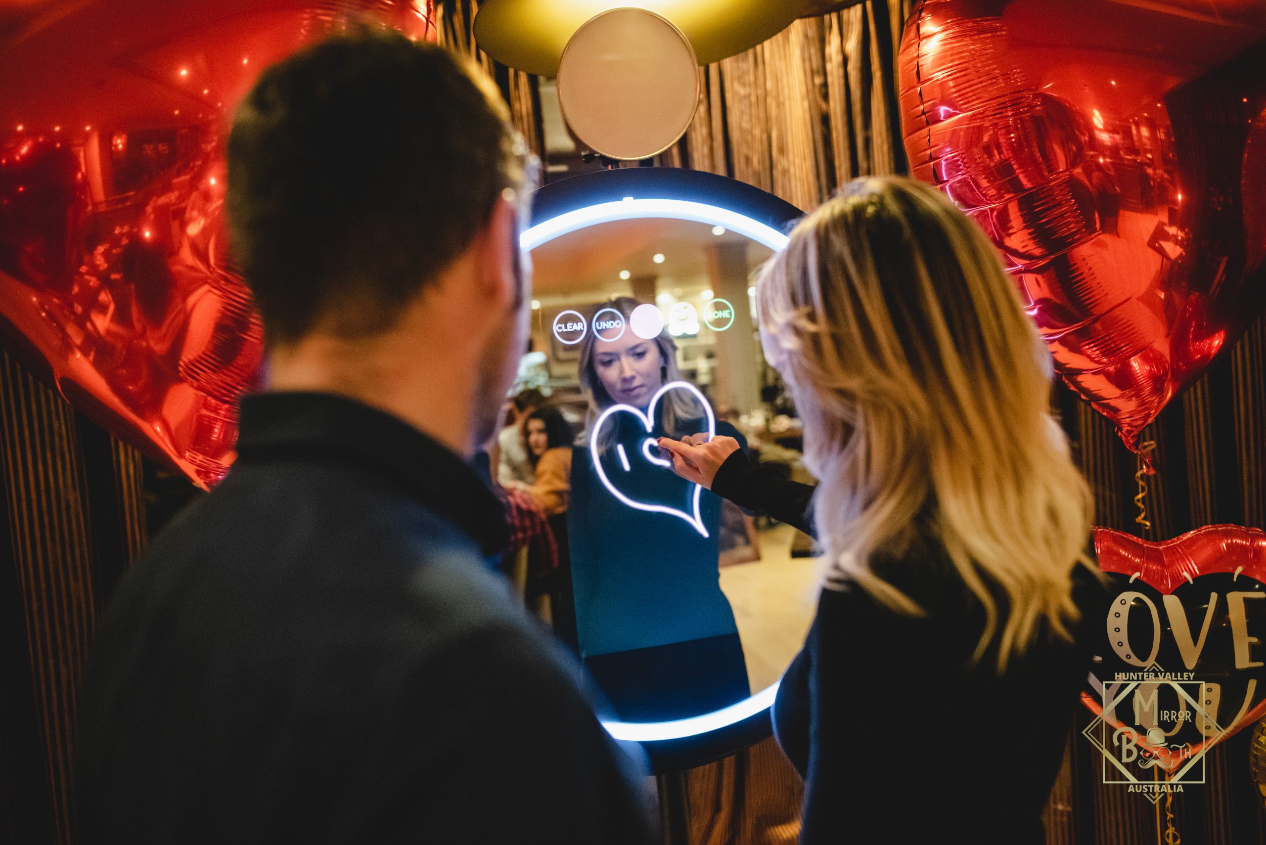 Couple drawing a heart animation the Beauty mirror surrounded by heart balloons